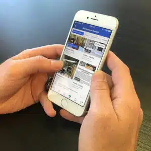 Corretor de imóveis segurando o celular sobre a mesa. Ele está acessando o marketplace do Facebook e vendo imóveis.