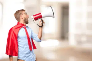 corretor de imóveis vestido de super herói com capa vermelha e um alto falante vermelho e branco para fazer anúncios encantadores para vender um imóvel.